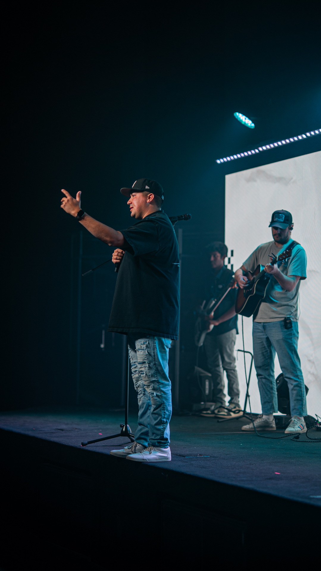 Alec Russo on stage holding a microphone with musicians behind him
